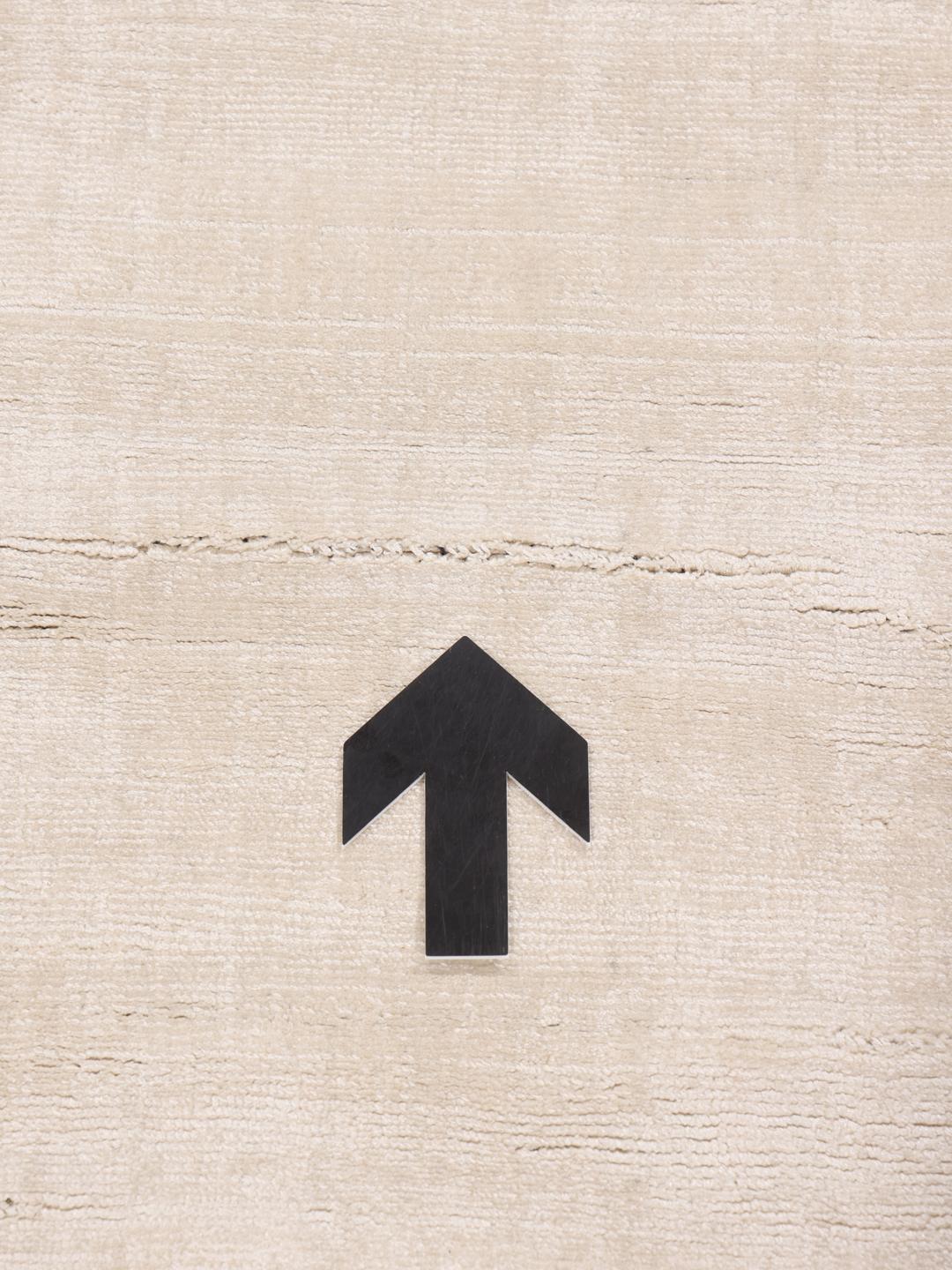Square beige rug with minimalist dark arrow accents