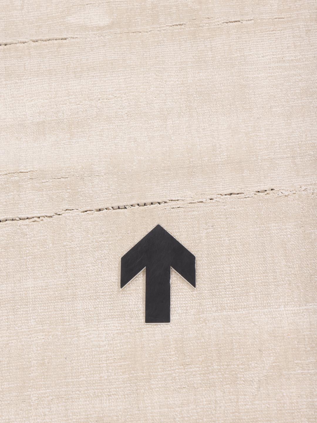 Square beige rug with minimalist dark arrow accents