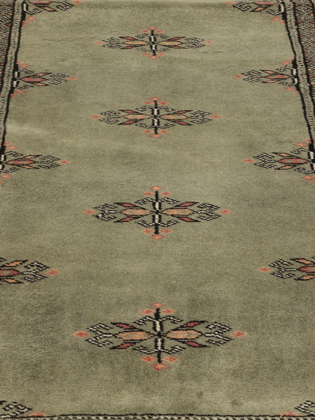 A long, hand-knotted Pakistan Bokhara runner rug in a soft sage green colour with repeating geometric motifs.