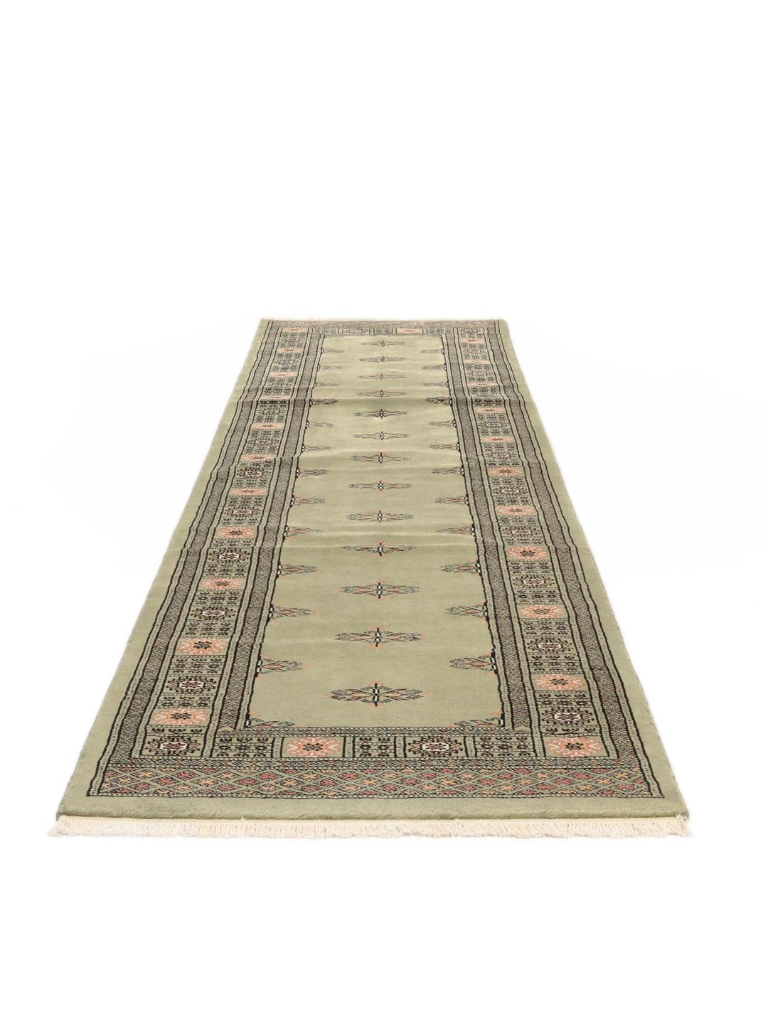 A long, hand-knotted Pakistan Bokhara runner rug in a soft sage green colour with repeating geometric motifs.