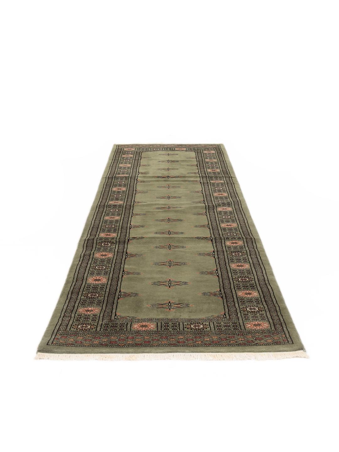 A long, hand-knotted Pakistan Bokhara runner rug in a soft sage green colour with repeating geometric motifs.