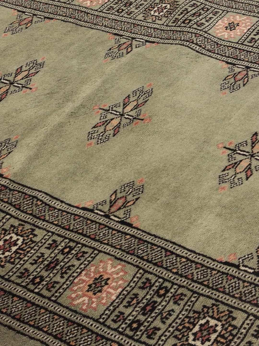 A long, hand-knotted Pakistan Bokhara runner rug in a soft sage green colour with repeating geometric motifs.