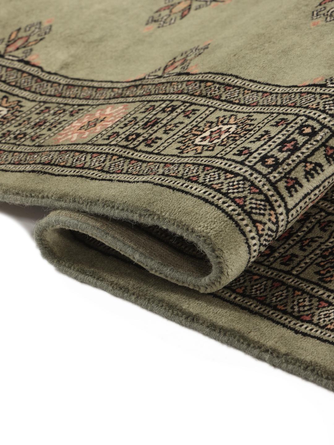 A long, hand-knotted Pakistan Bokhara runner rug in a soft sage green colour with repeating geometric motifs.