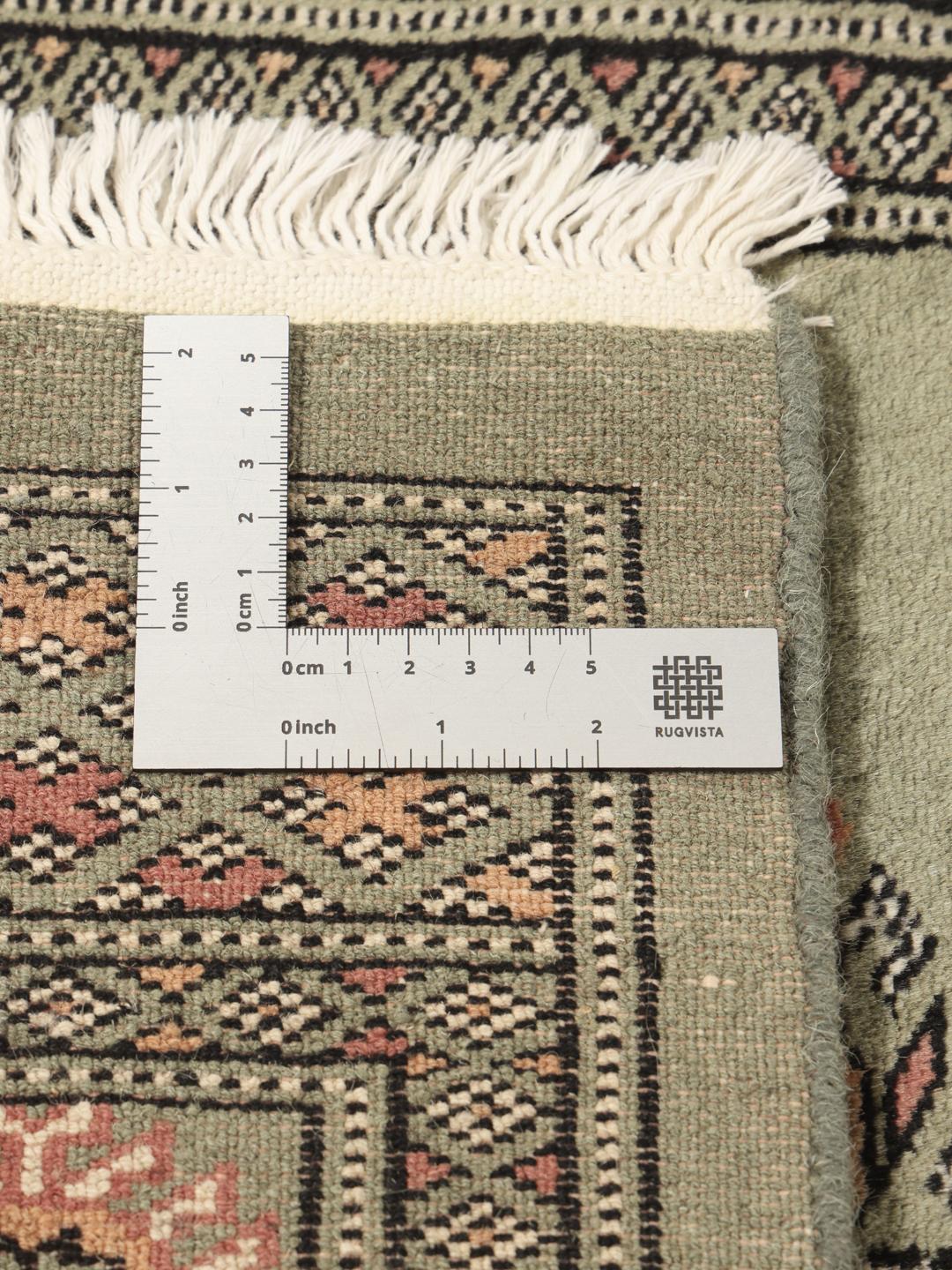 A long, hand-knotted Pakistan Bokhara runner rug in a soft sage green colour with repeating geometric motifs.