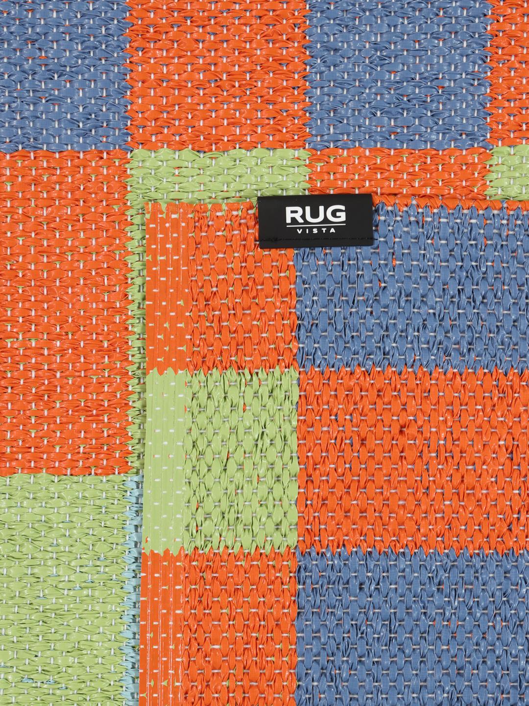 Un tapis rectangulaire présentant un motif à carreaux vibrant orange bleu et vert clair.