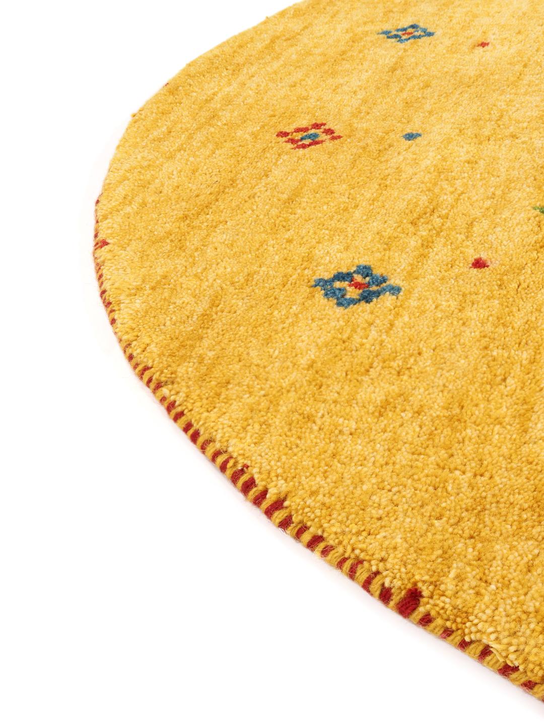 Rond geel tapijt met kleine kleurrijke motieven op een houten vloer