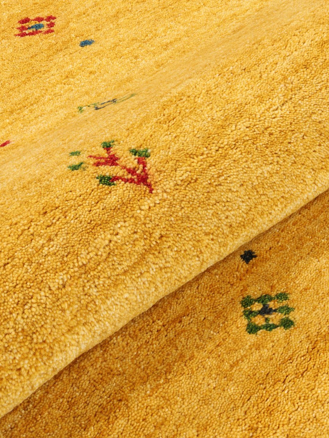 Rond geel tapijt met kleine kleurrijke motieven op een houten vloer