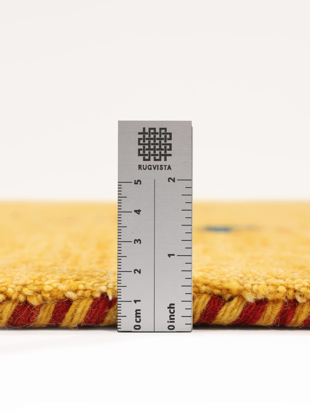 Een geel handgeknoopt wollen tapijt met kleine decoratieve tribale motieven.