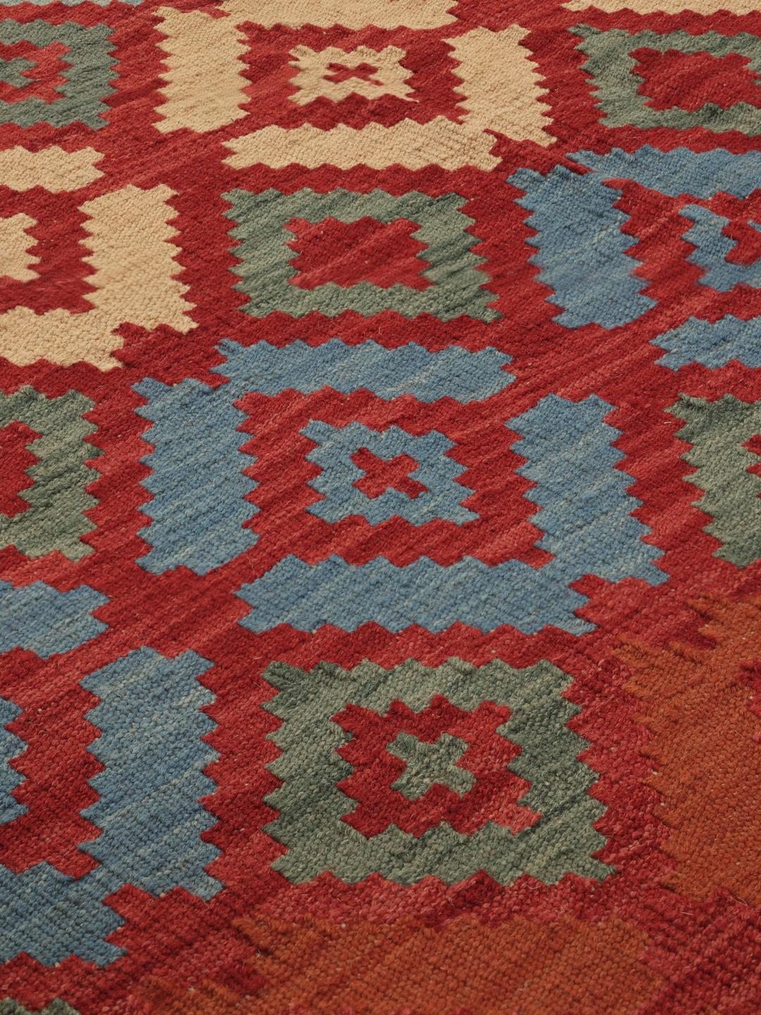Een handgeweven Kelim Ghashghai tapijt uit het Midden-Oosten in rode, blauwe en beige geometrische patronen.
