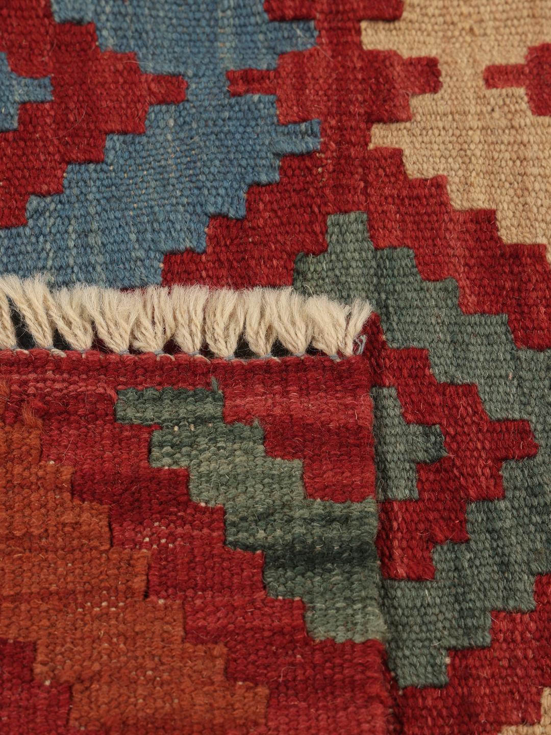 Een handgeweven Kelim Ghashghai tapijt uit het Midden-Oosten in rode, blauwe en beige geometrische patronen.