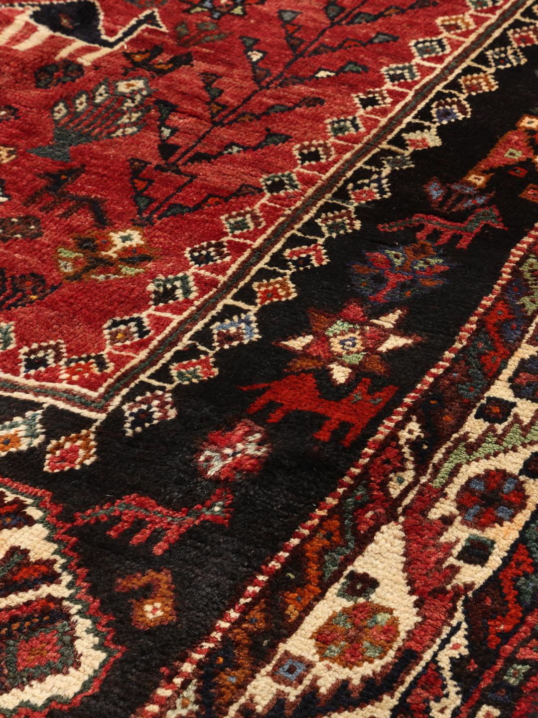 Hand-woven Shiraz rug from the Middle East featuring a vibrant red and black palette with tribal motifs