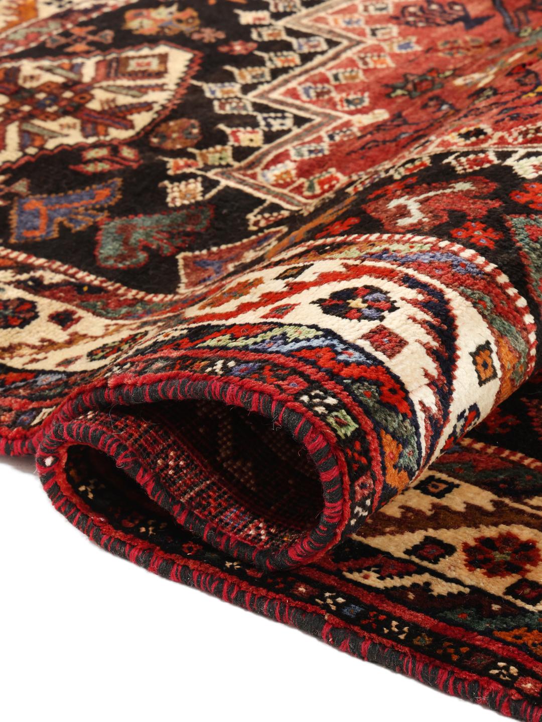 Hand-woven Shiraz rug from the Middle East featuring a vibrant red and black palette with tribal motifs