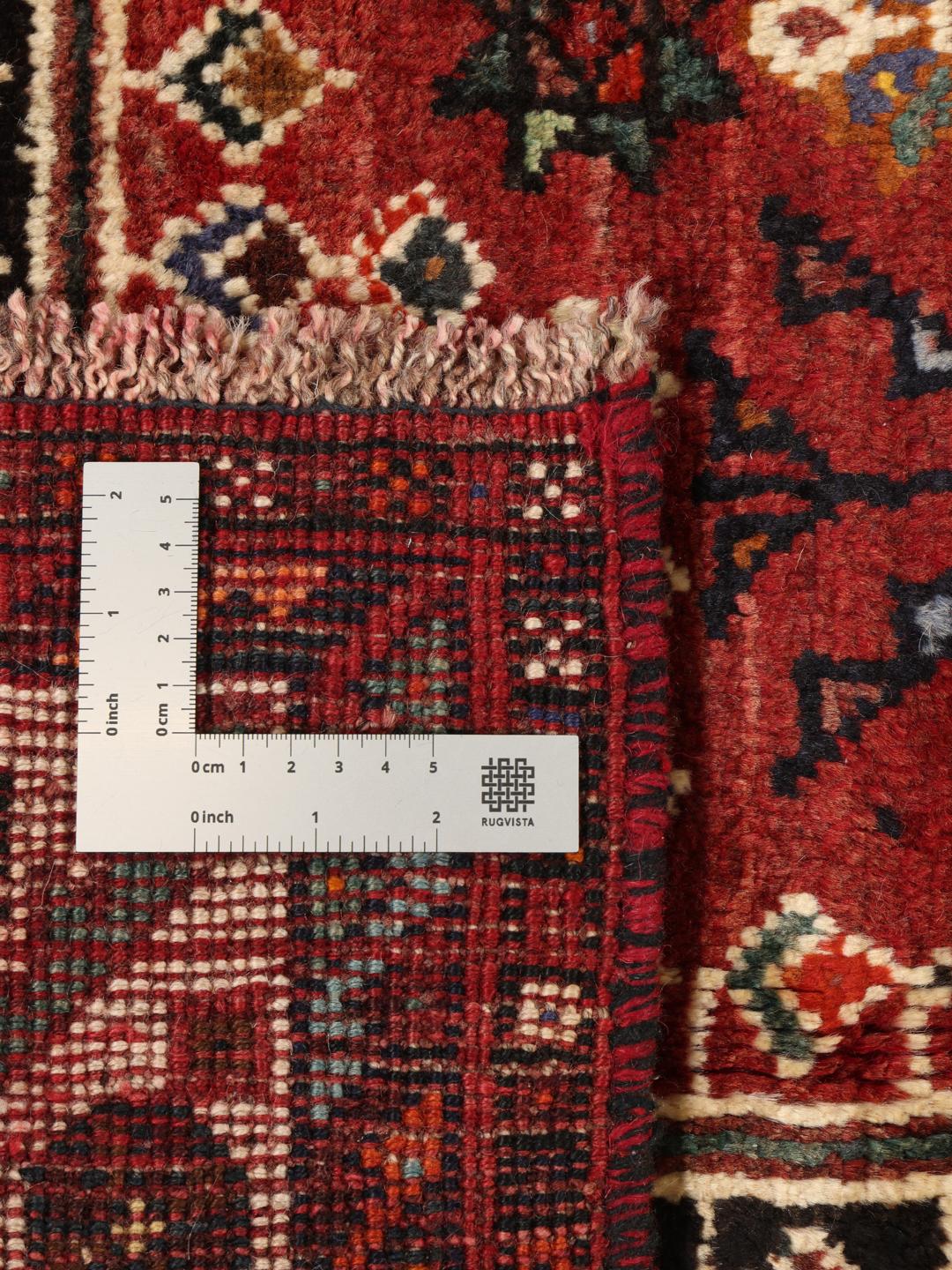 Hand-woven Shiraz rug from the Middle East featuring a vibrant red and black palette with tribal motifs