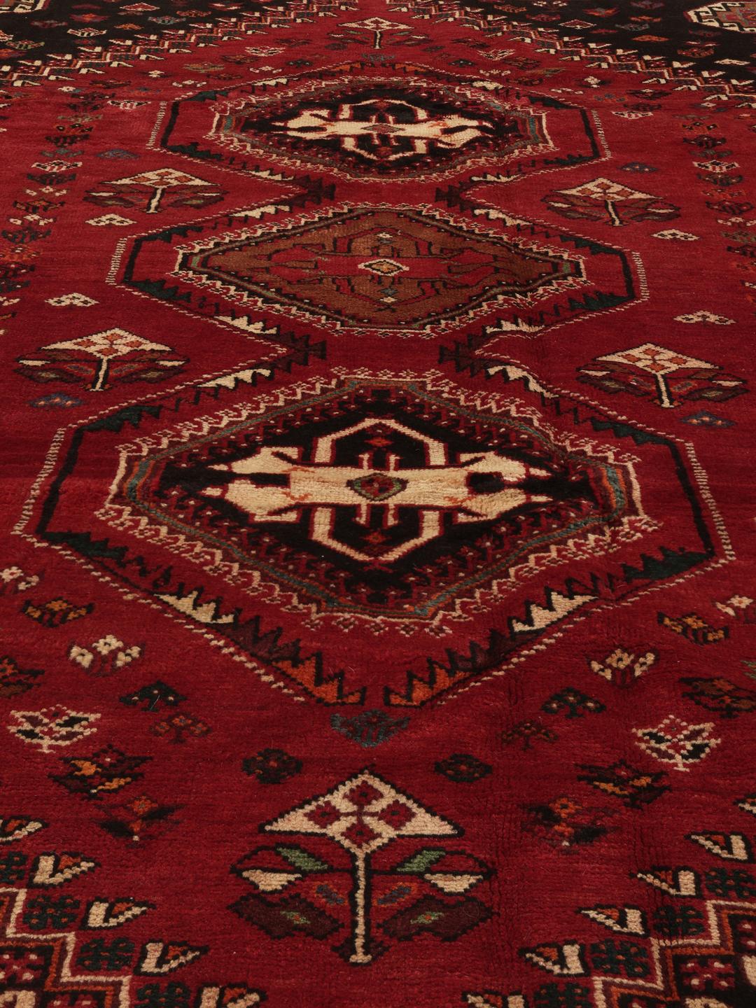 Hand-woven Shiraz rug from the Middle East featuring a vibrant red field and tribal motifs
