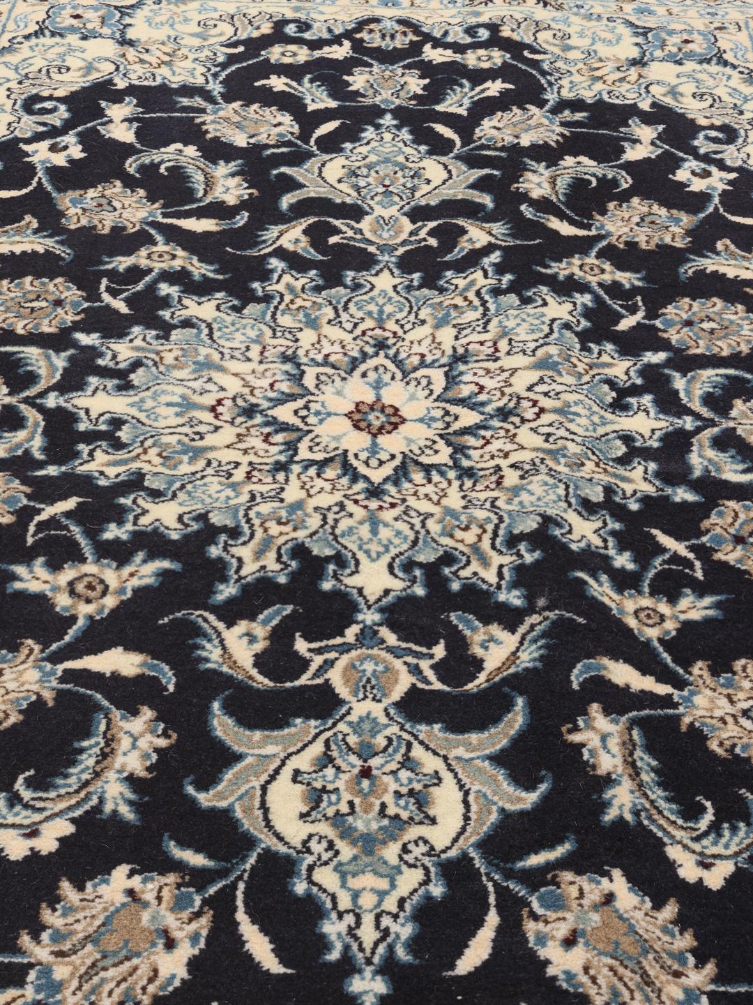 A hand-knotted Nain rug from the Middle East with a navy blue and cream floral medallion design.