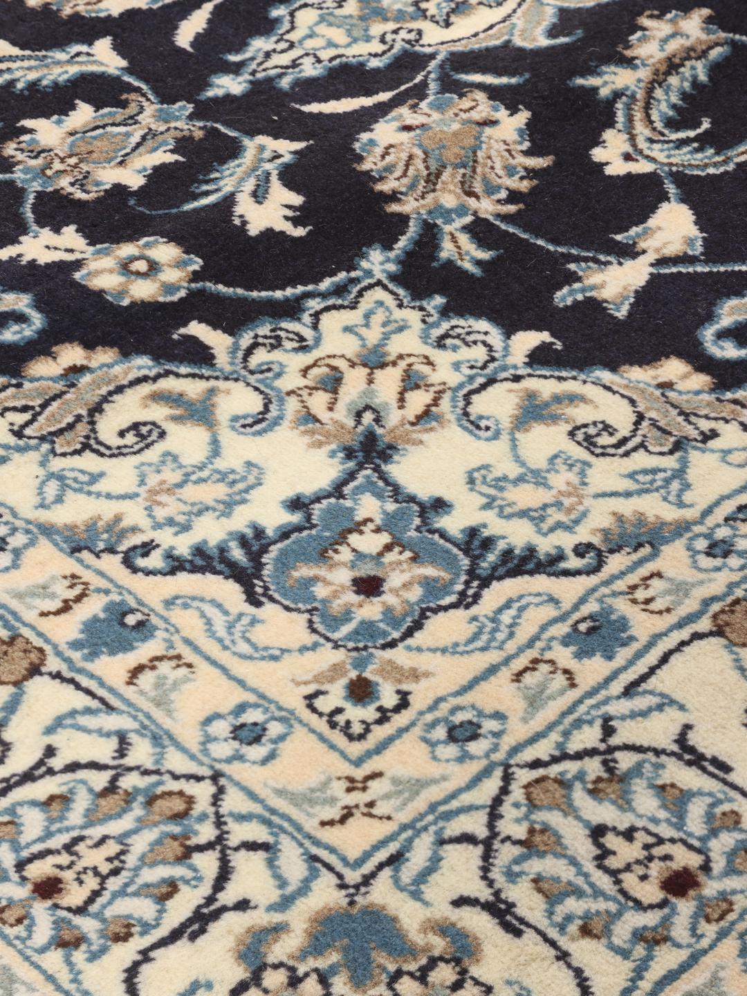 A hand-knotted Nain rug from the Middle East with a navy blue and cream floral medallion design.