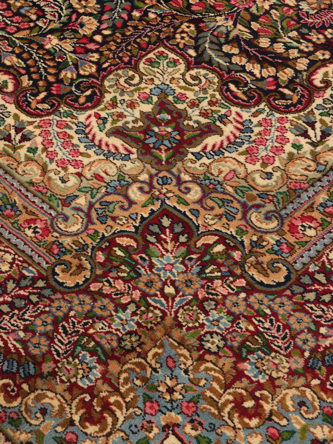 A large, rectangular Kerman rug from the Middle East featuring a complex red and dark red floral medallion pattern.