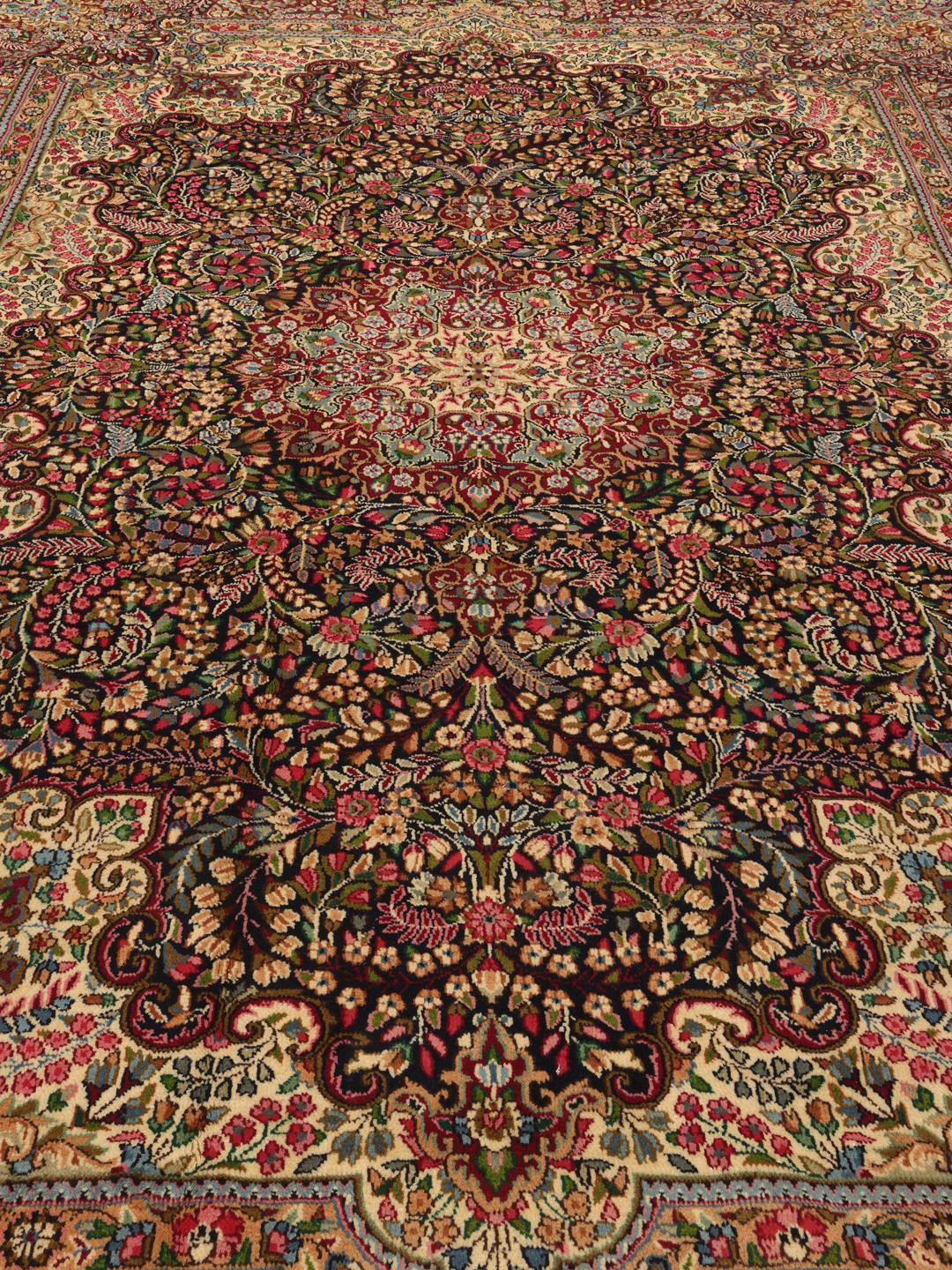 A large, rectangular Kerman rug from the Middle East featuring a complex red and dark red floral medallion pattern.
