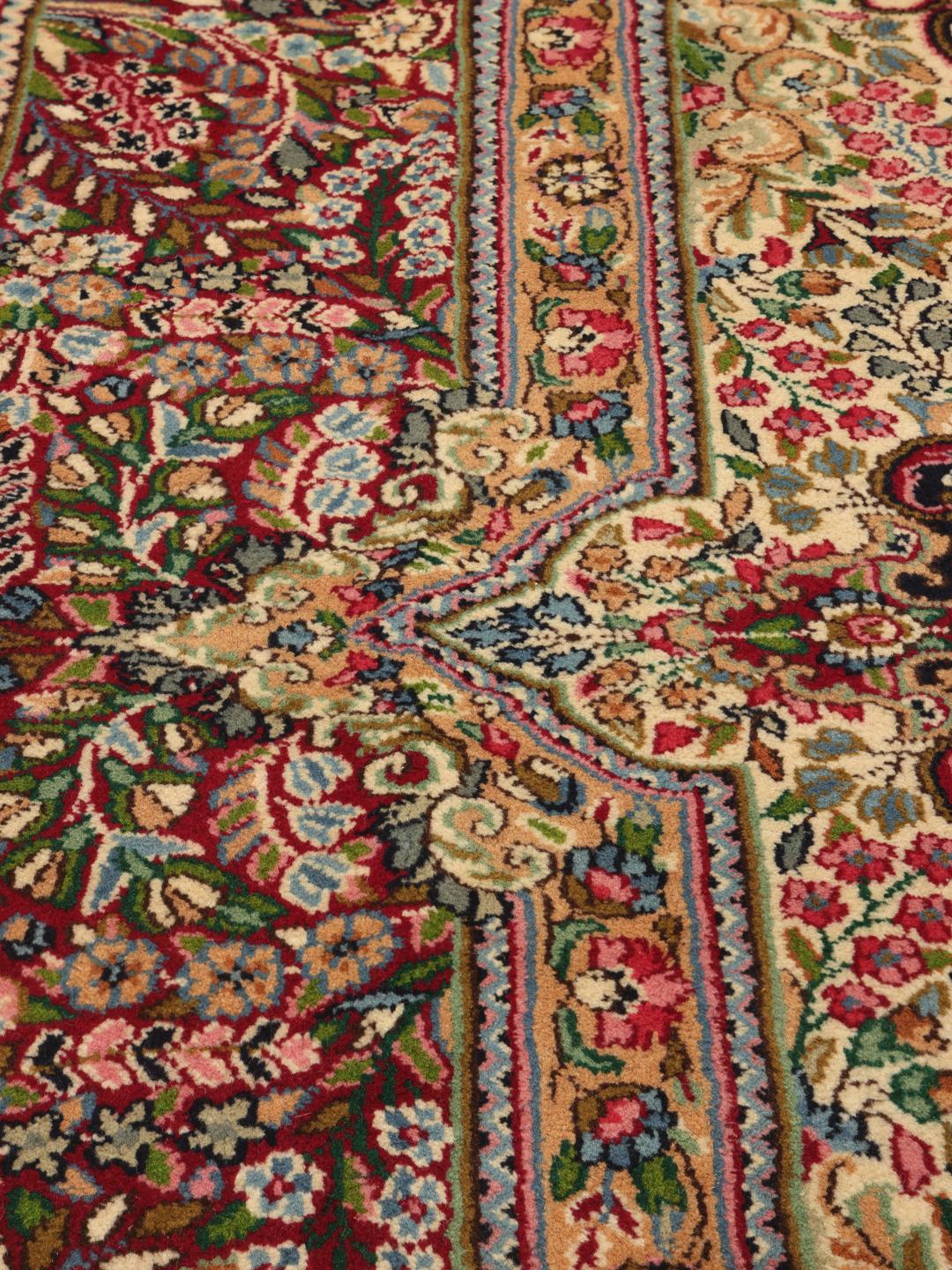 A large, rectangular Kerman rug from the Middle East featuring a complex red and dark red floral medallion pattern.
