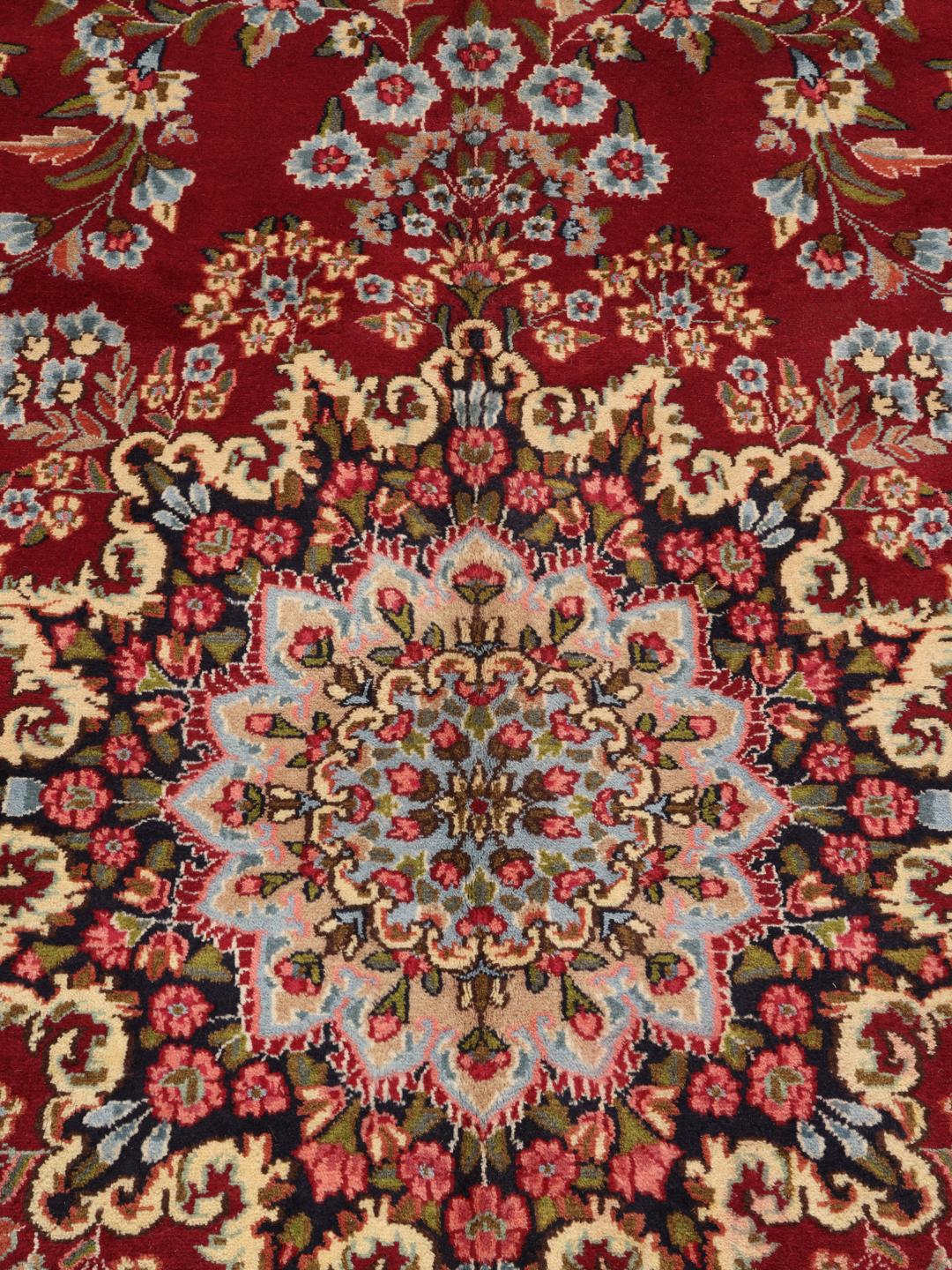 A hand-knotted Kerman rug with a large central floral medallion on a red field.