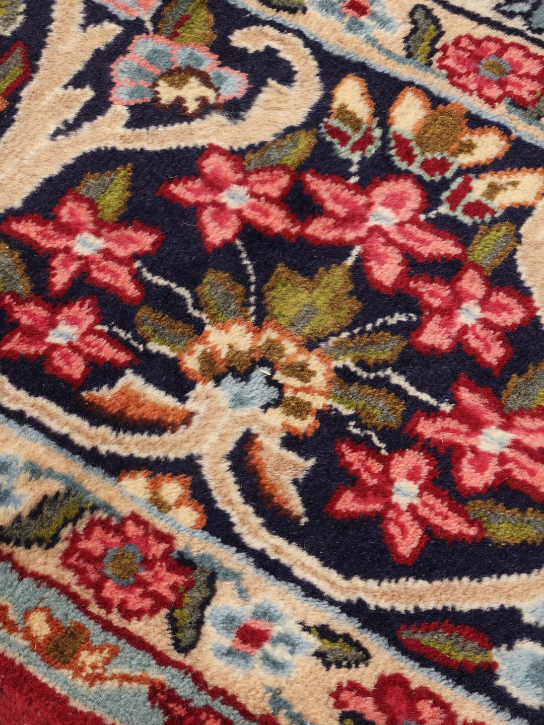 A hand-knotted Kerman rug with a large central floral medallion on a red field.