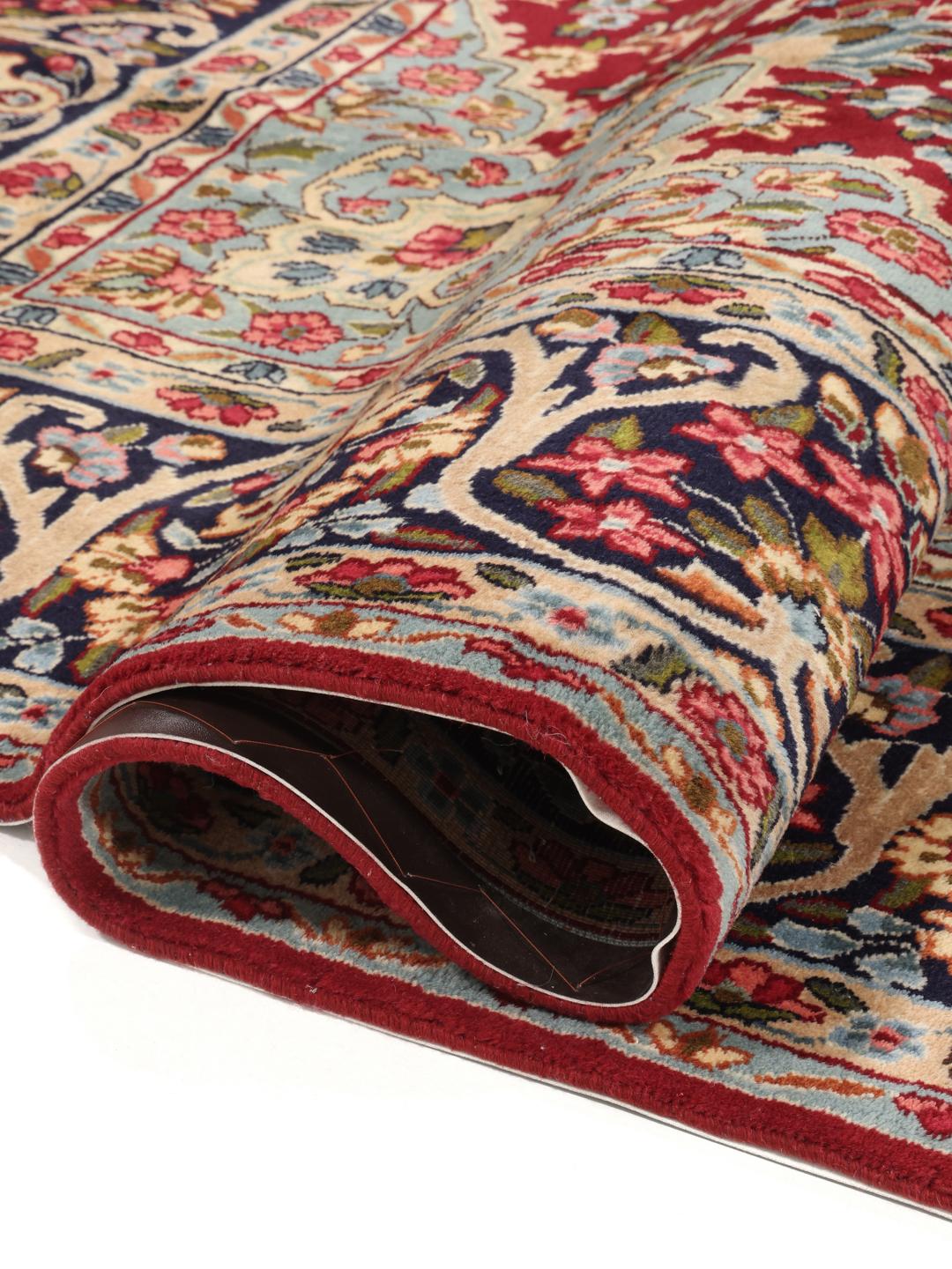 A hand-knotted Kerman rug with a large central floral medallion on a red field.