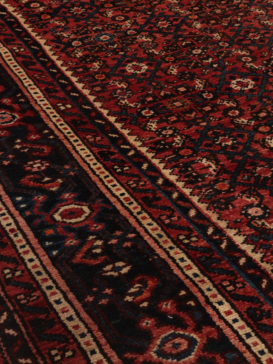 A hand-knotted Hosseinabad rug featuring a traditional dark-red field and detailed patterns.