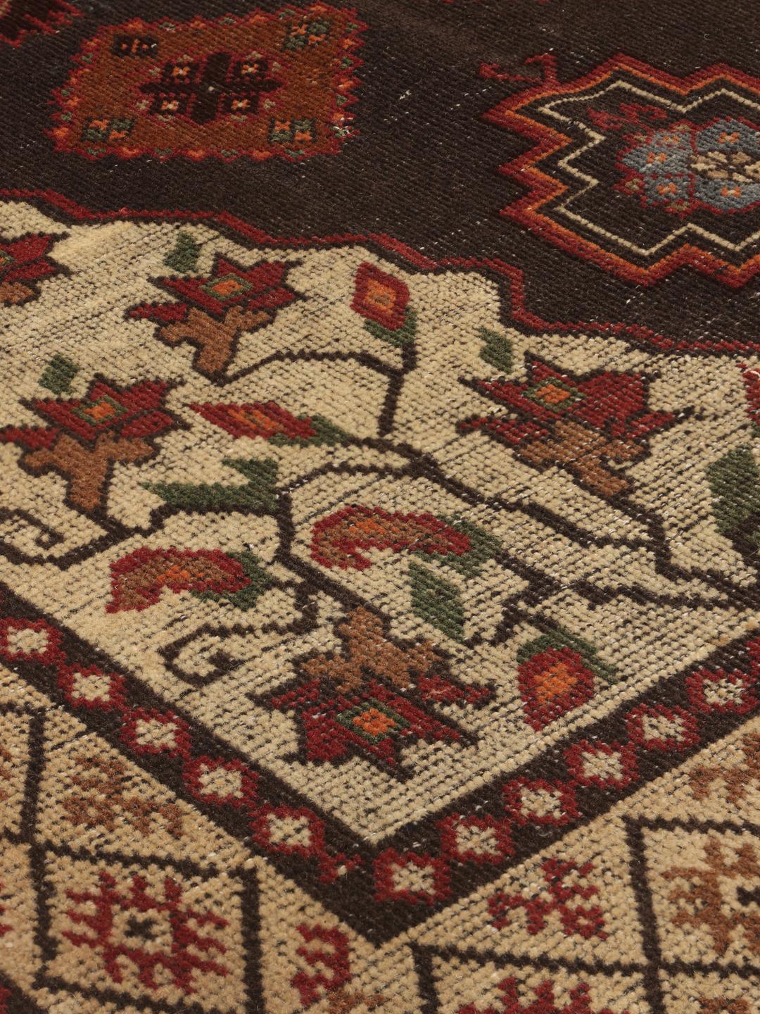 Een handgeknoopt tapijt uit het Midden-Oosten met een donker centraal medaillon en bloemrijke hoeken in tinten rood, beige en blauw.