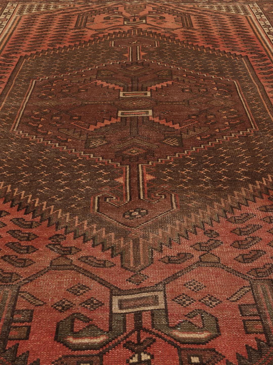 Et håndknyttet Hamadan-tæppe fra Mellemøsten med geometriske mønstre i mørkerøde og brune toner.