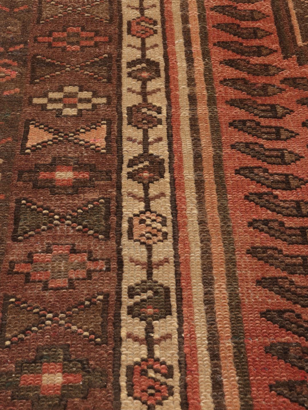Et håndknyttet Hamadan-tæppe fra Mellemøsten med geometriske mønstre i mørkerøde og brune toner.