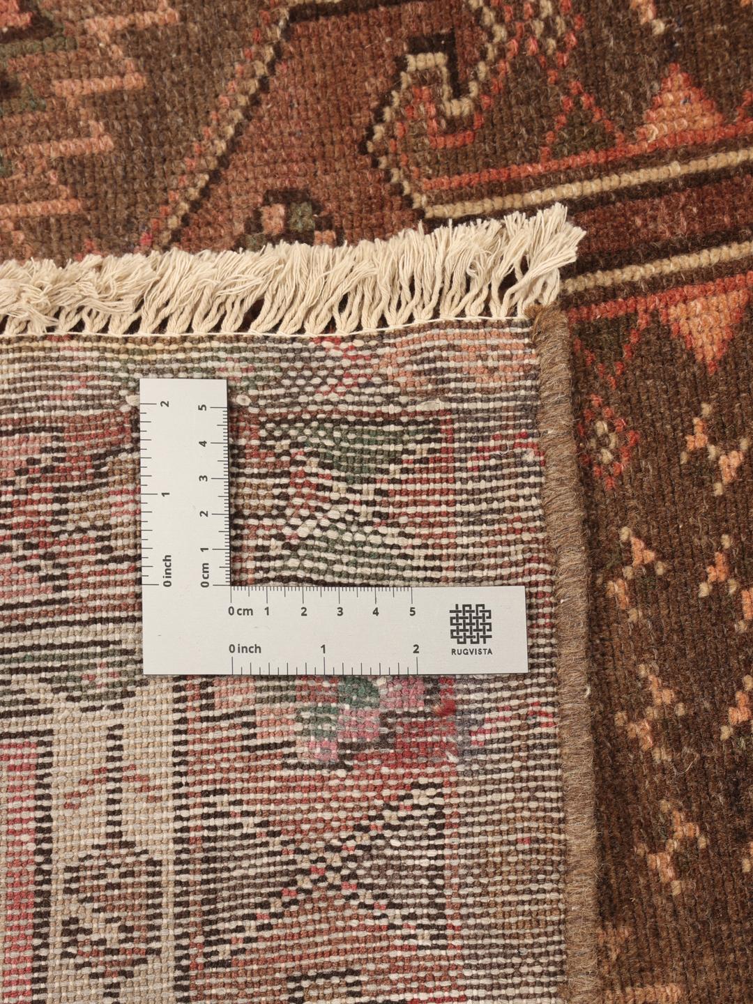 Et håndknyttet Hamadan-tæppe fra Mellemøsten med geometriske mønstre i mørkerøde og brune toner.