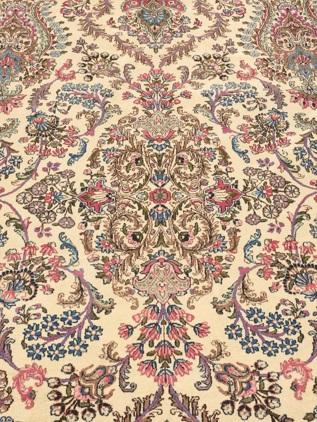 A large hand-knotted Middle Eastern Kerman rug with intricate floral patterns in beige and pink.