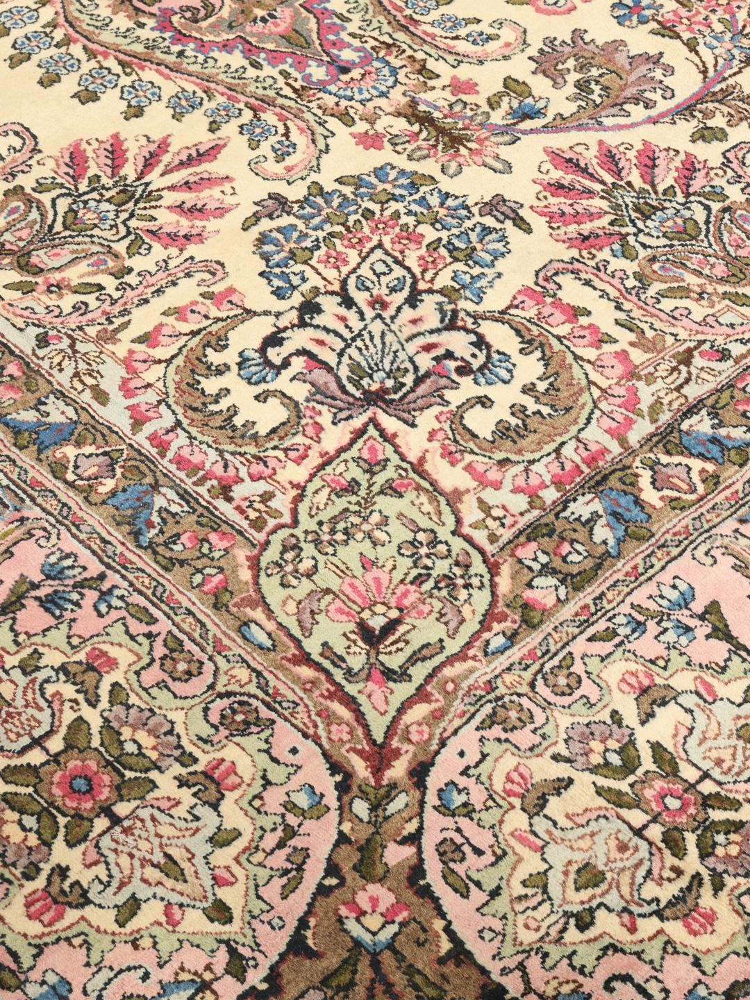 A large hand-knotted Middle Eastern Kerman rug with intricate floral patterns in beige and pink.
