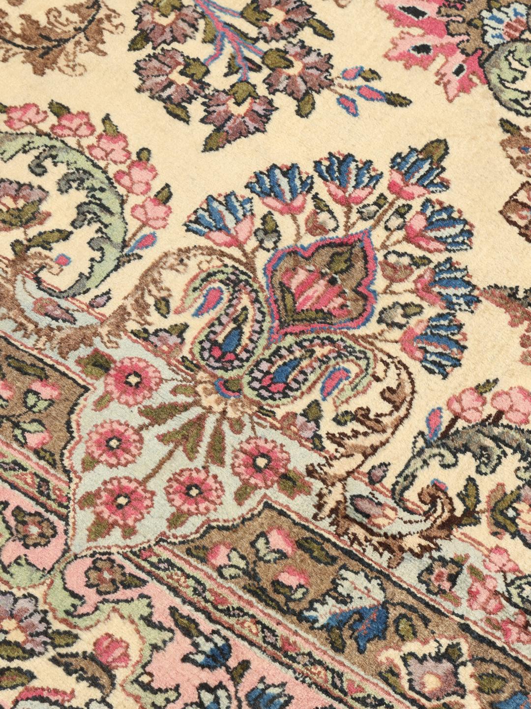 A large hand-knotted Middle Eastern Kerman rug with intricate floral patterns in beige and pink.