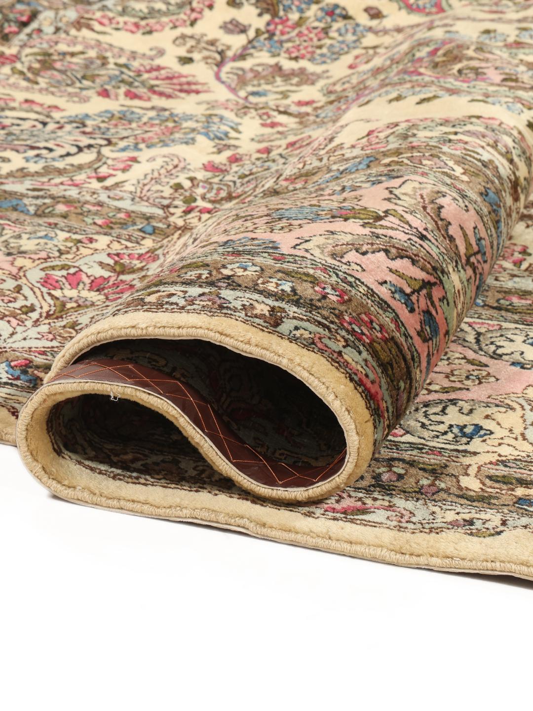 A large hand-knotted Middle Eastern Kerman rug with intricate floral patterns in beige and pink.
