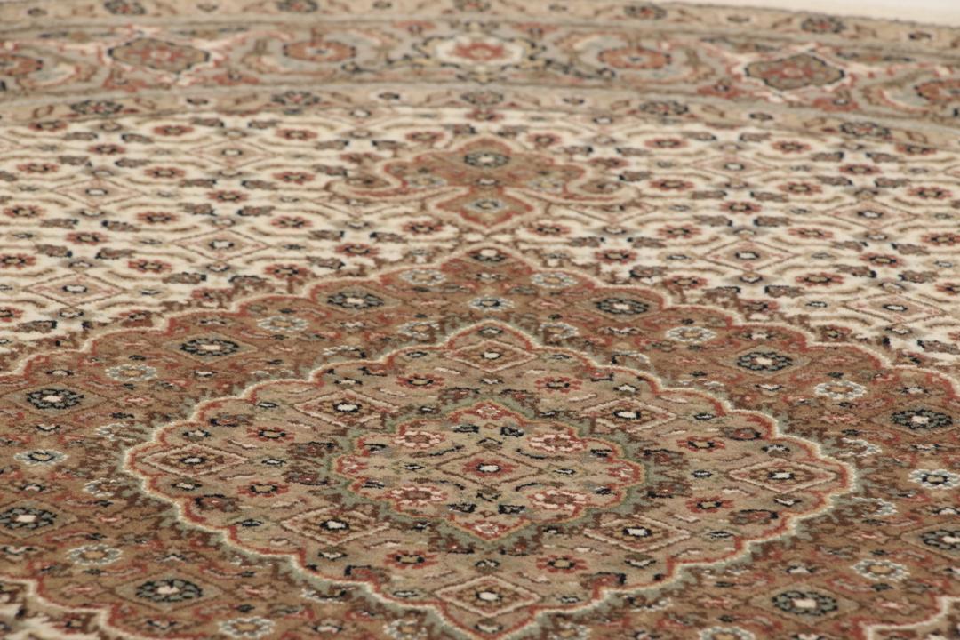 Rundt Tabriz-tæppe med indviklede mønstre i beige, brun og rød, håndlavet i Indien.