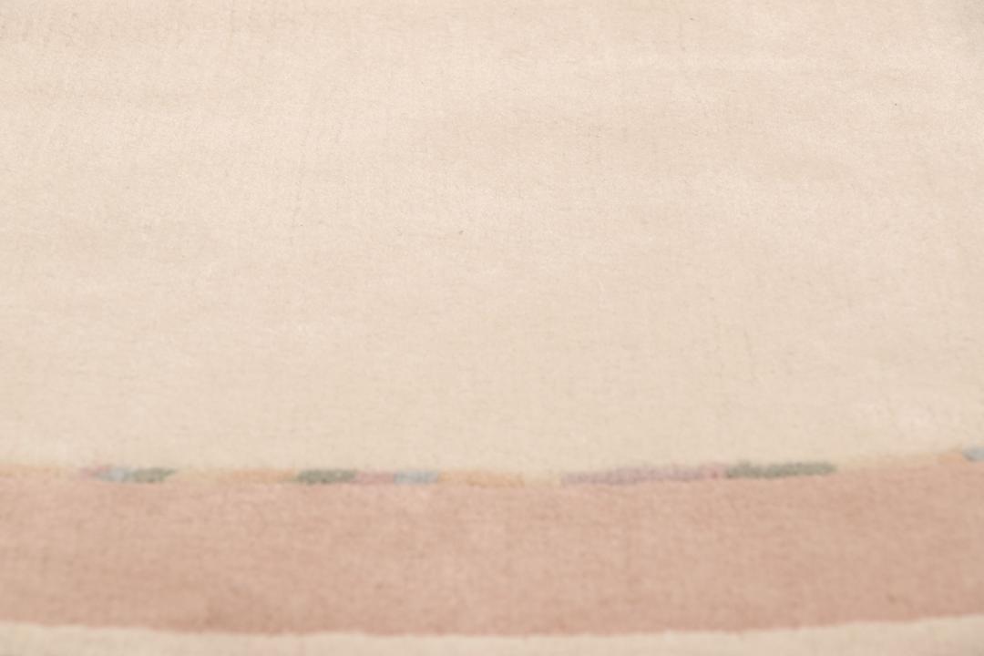 Een rond, uniek Wool tapijt uit Nepal met een minimalistisch beige en zachtroze ontwerp.