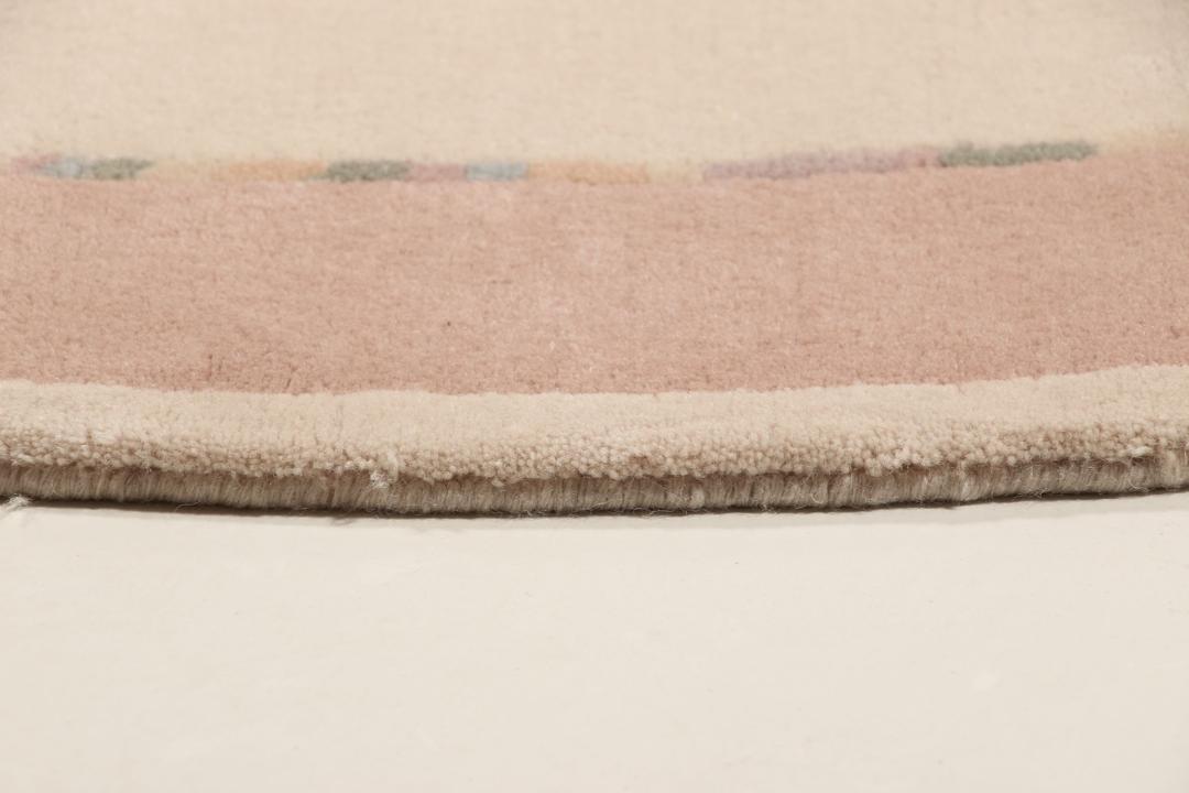 Een rond, uniek Wool tapijt uit Nepal met een minimalistisch beige en zachtroze ontwerp.
