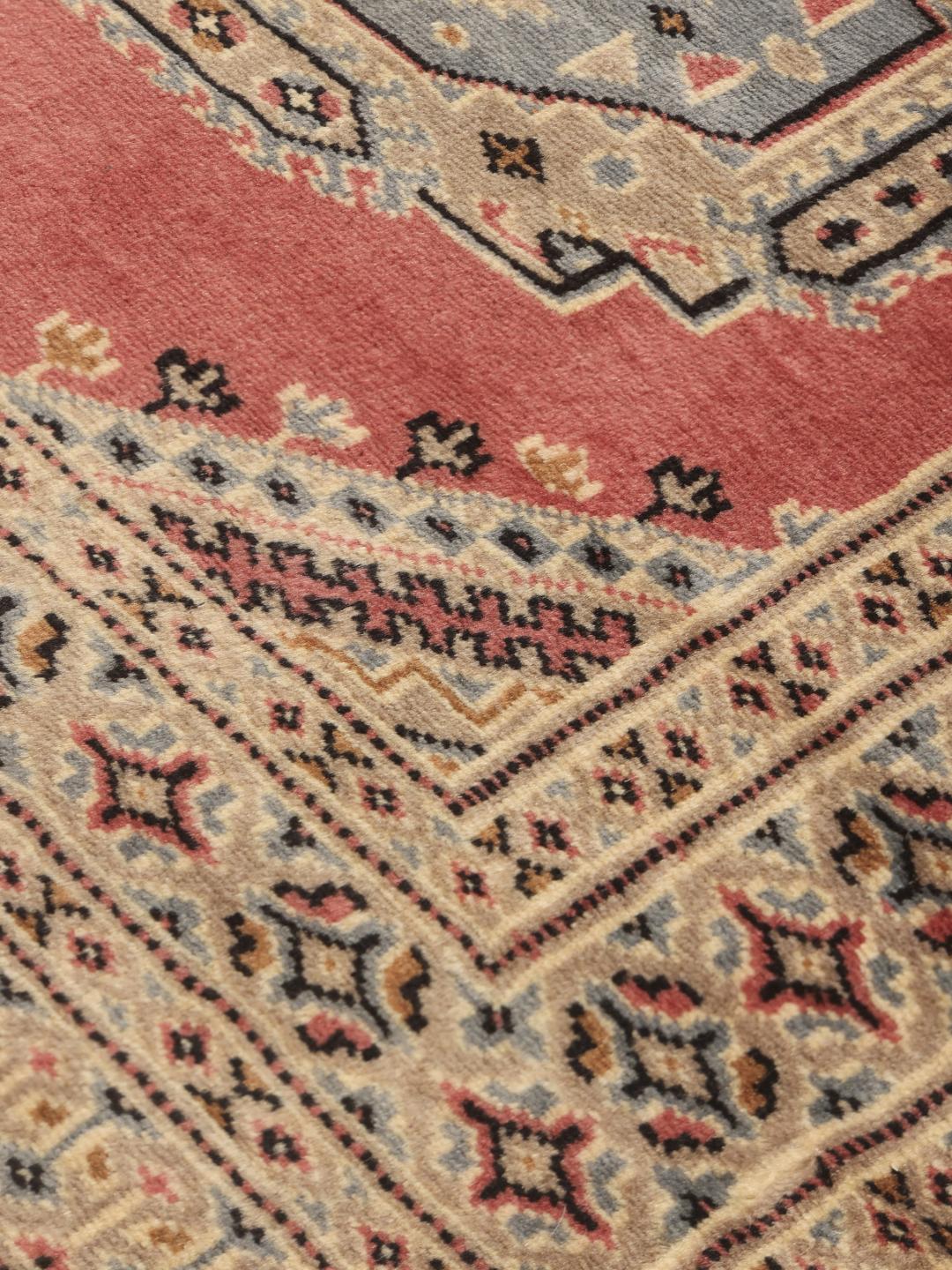 Hand-knotted Pakistan Bokhara rug with a red field and traditional medallion patterns.