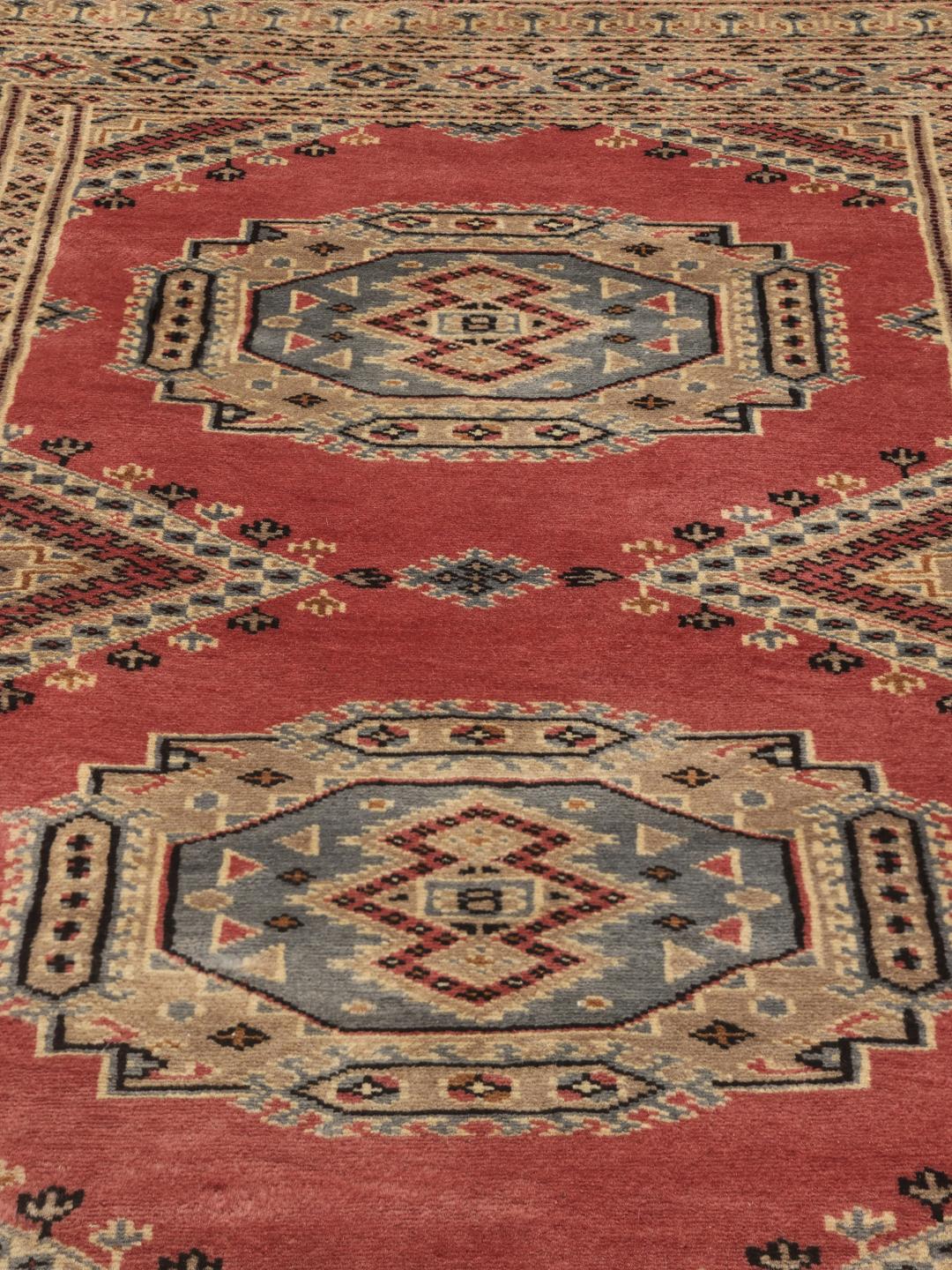 Hand-knotted Pakistan Bokhara rug with a red field and traditional medallion patterns.