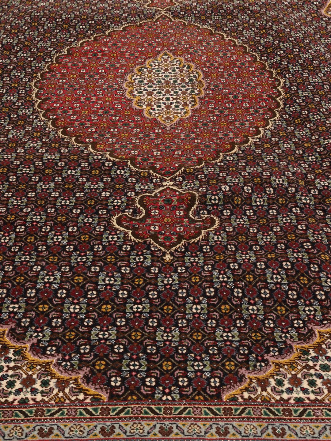 Et håndknyttet Tabriz-tæppe fra Mellemøsten med en mørkerød bund og et detaljeret medaljondesign.