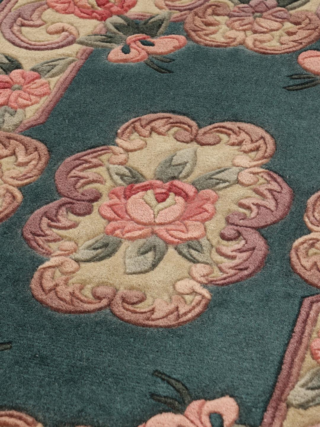 Et rektangulært uldtæppe fra Kina med en teal baggrund og lyserøde blomstermønstre.