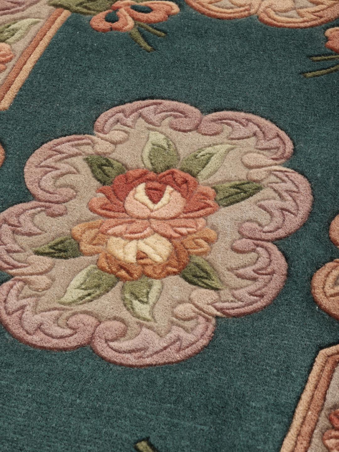 Et håndknyttet blomstret tæppe fra Kina med en petroleumsfarvet baggrund og blomstermotiver i pastelfarver.