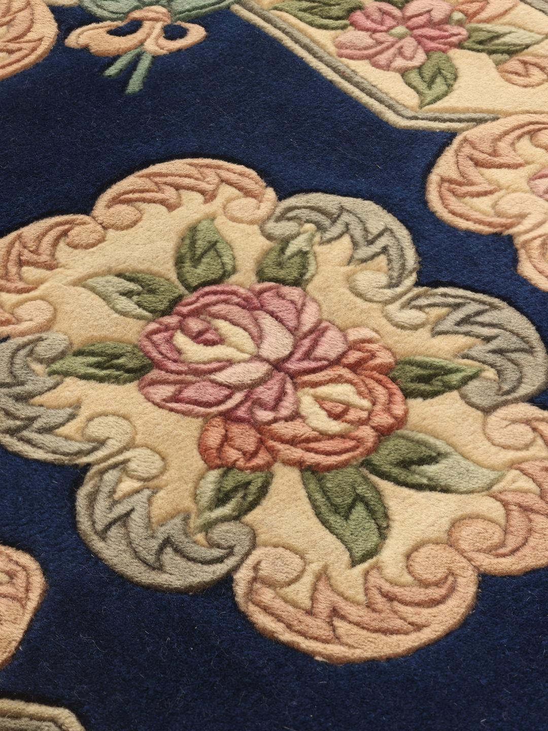 Et rektangulært håndknyttet kinesisk tæppe med en blå bund og blomstermønster.