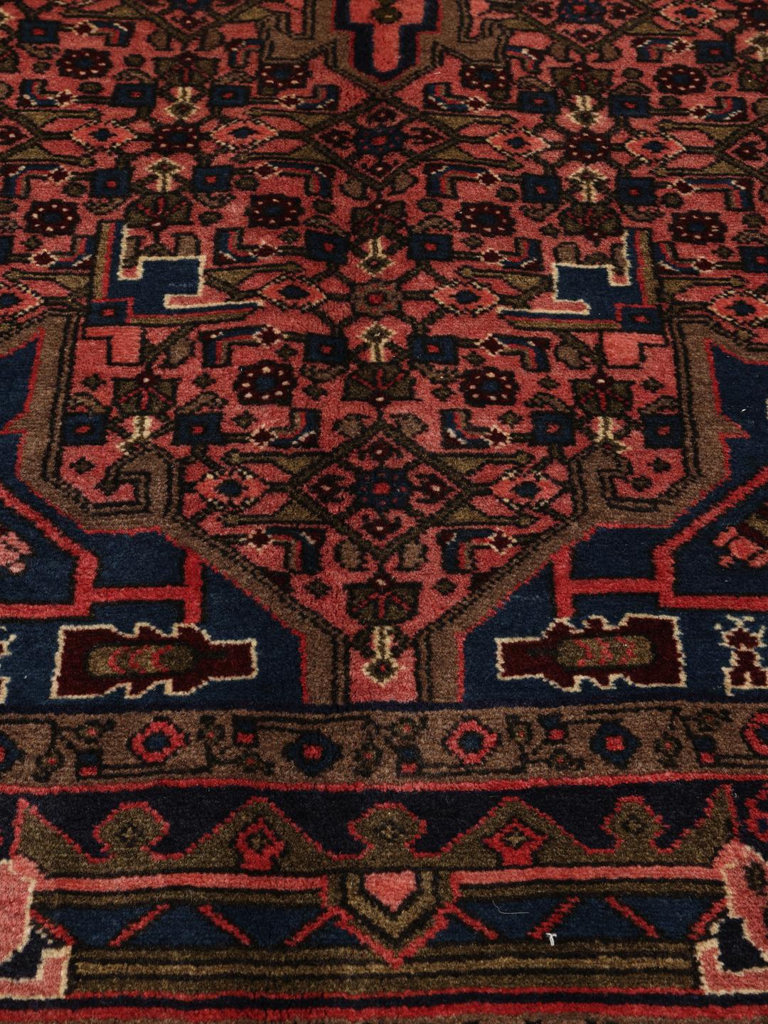 Een handgeknoopt Koliai-tapijt uit het Midden-Oosten met een donkerblauw en rood kleurenpalet.