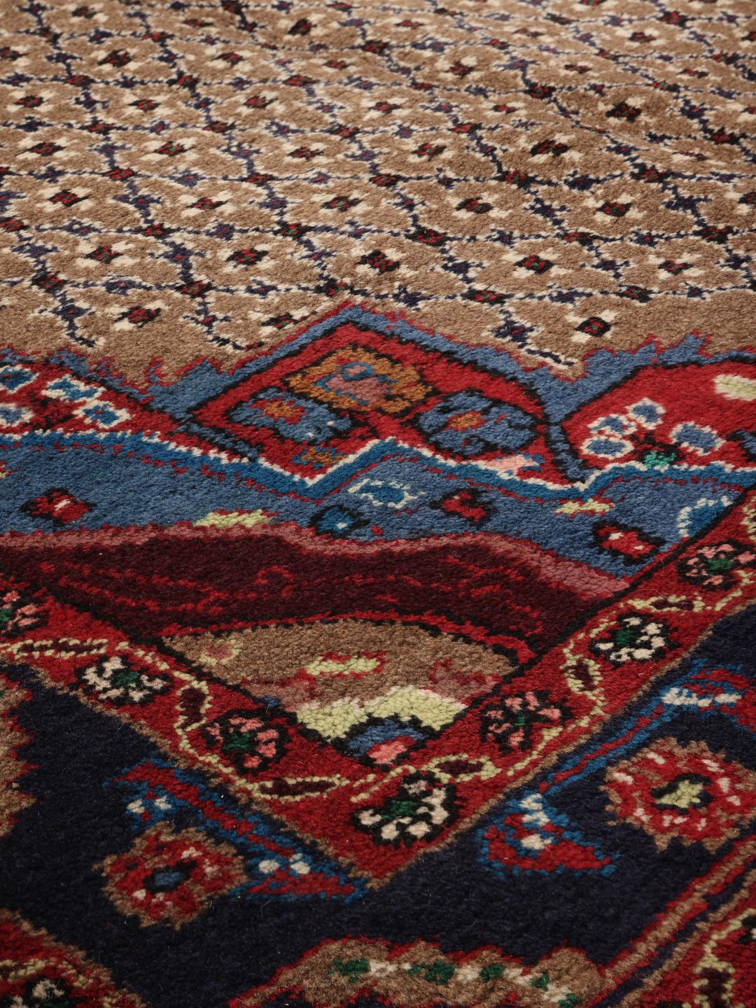 Un tapis Koliai noué à la main avec un médaillon central sur un fond beige et des bordures rouge foncé et bleu