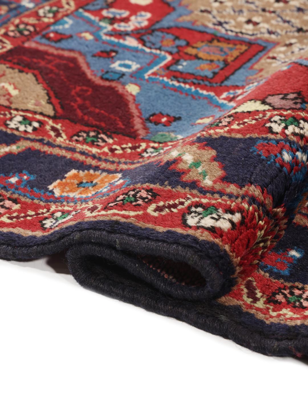 Un tapis Koliai noué à la main avec un médaillon central sur un fond beige et des bordures rouge foncé et bleu