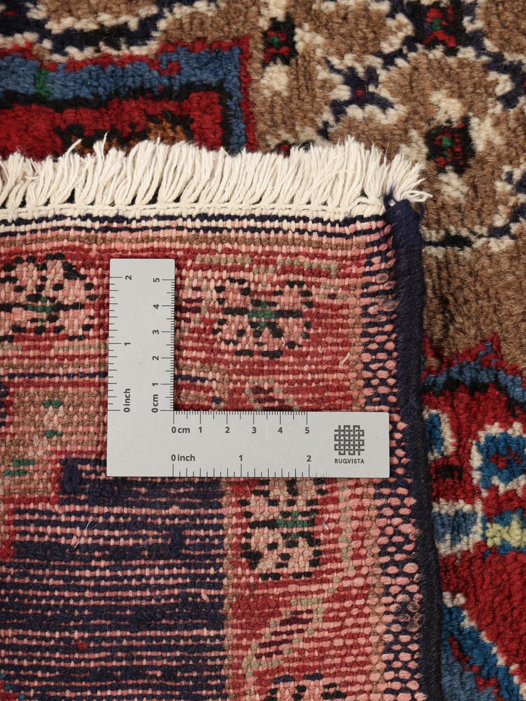 Un tapis Koliai noué à la main avec un médaillon central sur un fond beige et des bordures rouge foncé et bleu