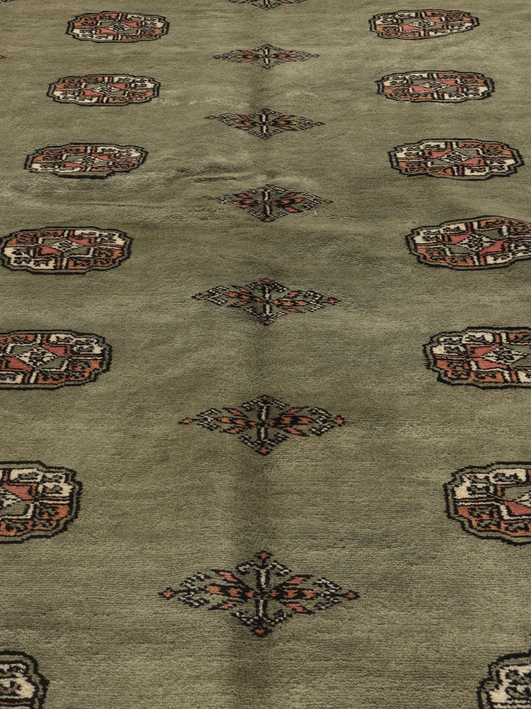 A hand-knotted green Pakistan Bokhara rug with traditional repeating motifs.