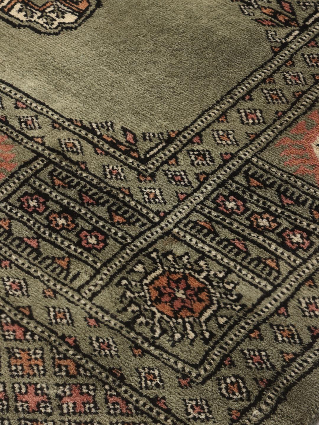 A hand-knotted green Pakistan Bokhara rug with traditional repeating motifs.